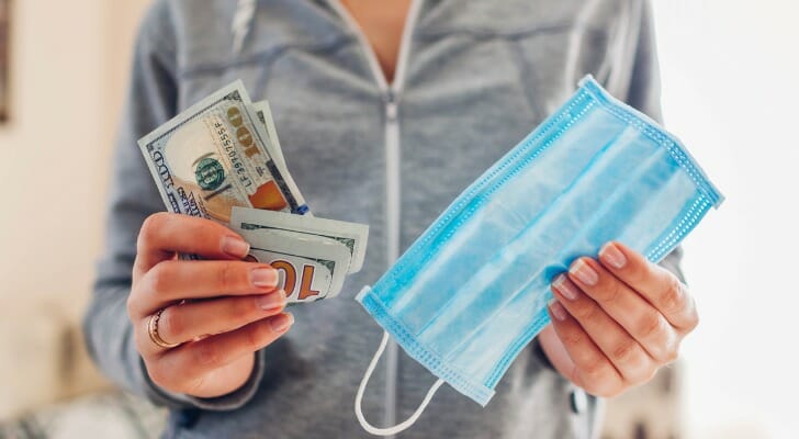 Woman holding $100 bills and a face mask