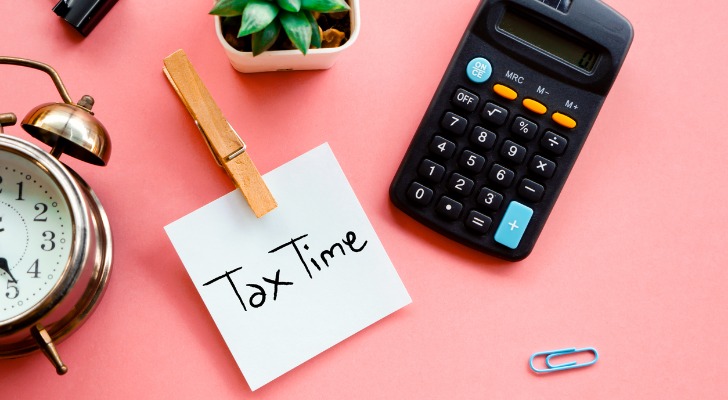 Image shows a post-it on a desk, next to a desk plant, calculator and other office supplies. The post-it reads, "Tax Time." It's important to understand capital tax rates in your state when going over investment taxes.