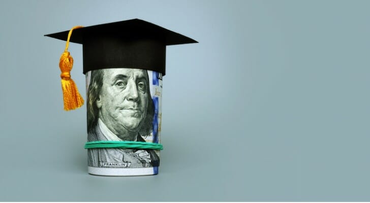 Roll of $100 bills with a college graduation cap on top