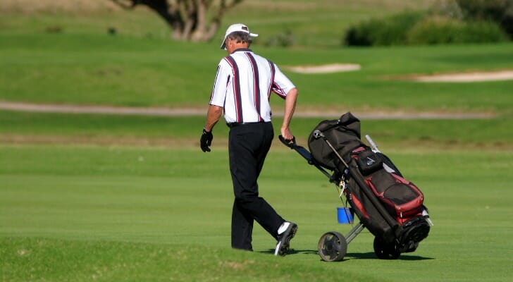 A retired man strolls down a golf course fairway.