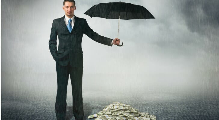 Man holds umbrella over a pile of money