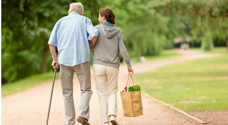 A caregiver walks alongside a man in a park. A retirement strategy known as the Social Security bridge is one way to create an enlarged stream of guaranteed income without an annuity. 