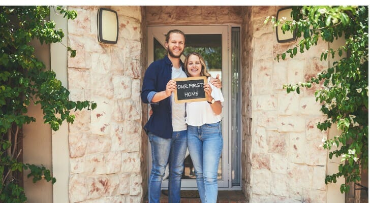 A young couple standing in front of their first house