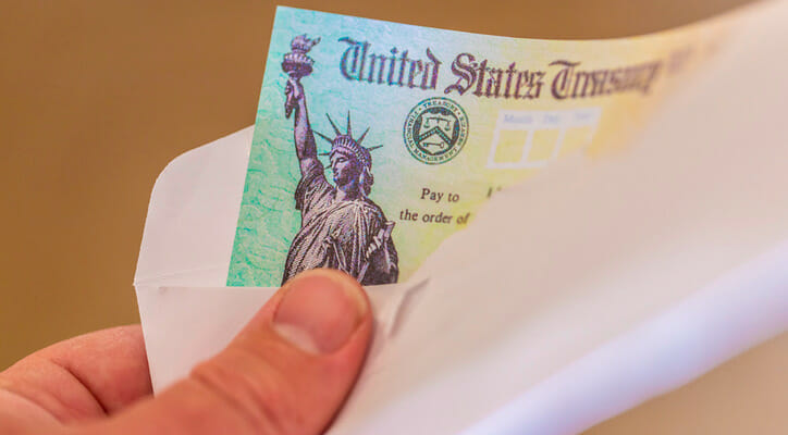 Image shows a hand holding an envelope from which a check from the U.S. Treasury is partially visible. SmartAsset analyzed Census data to conduct its latest study on the cities where retirees rely most on Social Security.