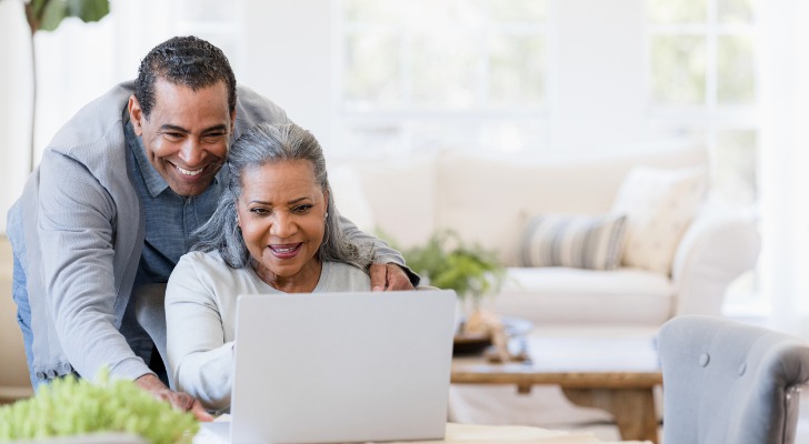 husband-looks-over-wifes-shoulder-at-grandchildrens-photos-on-laptop-SmartAsset