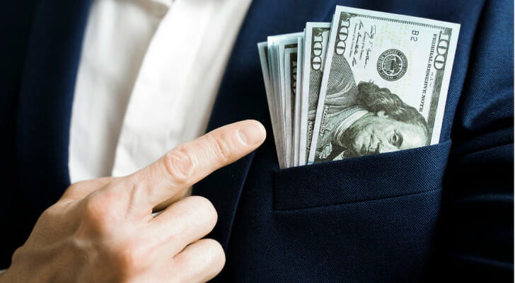 Image shows a stack of $100 bills in the front pocket of a person's blazer, with the person's finger pointing to the money. SmartAsset used IRS data to conduct the latest edition of its study on the states with the largest increases in million-dollar earners.