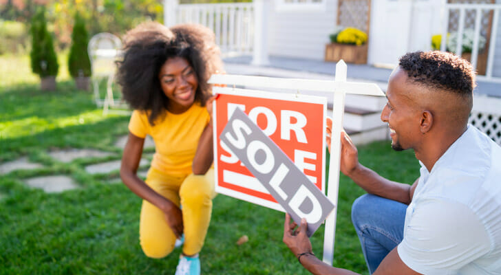 Image shows two relatively young people changing the sign outside their home from "For Sale" to "Sold. SmartAsset found the places where more young residents are buying homes, based on 2009 and 2019 homeownership rates among residents younger than 35.