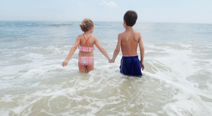 Young brother and sister holding hands as they walk into the surf on a Delaware beach
