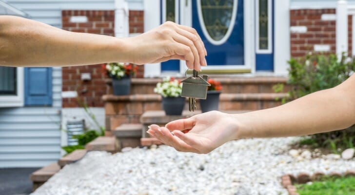 Image shows one person's hand placing the key to a new home in a second person's hand; the front porch of the new home is in the background. SmartAsset analyzed various data sources to find out how long it takes renters to become homeowners.