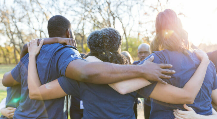 Image shows a group of volunteers huddled together at the beginning of a charity event. SmartAsset analyzed key metrics related to giving and volunteering to conduct its latest study on the places where Americans give the most to charity.