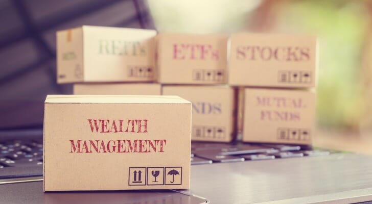 Image shows several cardboard boxes with various labels. Four boxes in the background are labeled "REITs," "ETFs," STOCKS" and "MUTUAL FUNDS." The one box in the foreground is labeled "WEALTH MANGEMENT."