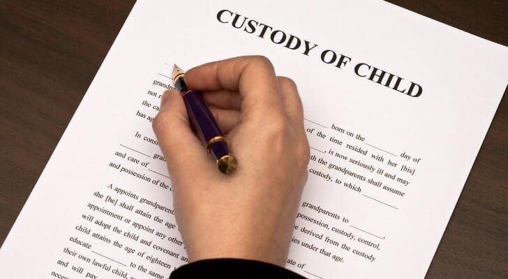 Image shows a hand holding a pen above a document titled "Custody of Child." Custody and guardianship are similar concepts but have important differences.