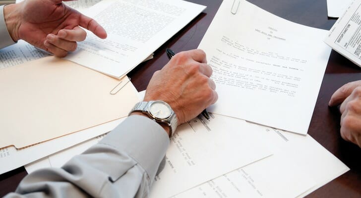 Image shows someone's hand preparing to sign the estate planning documents in front of them.