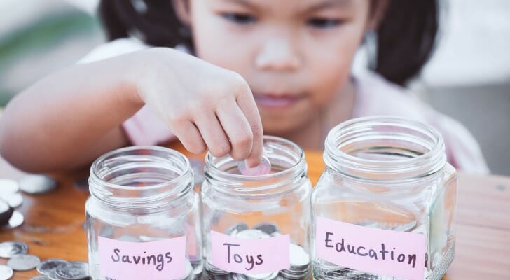 Image shows a child sitting in front of three jars with coins in each; the jars are labeled "Savings," "Toys" and "Education."