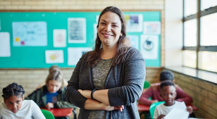 图象显示站立在教室前面的一位女性老师坐在书桌的学生。伟德ios appSmartAsset看一下各种数据来源，以完成今年的他们的学习版本，以成为一名教师的最佳美国地区。