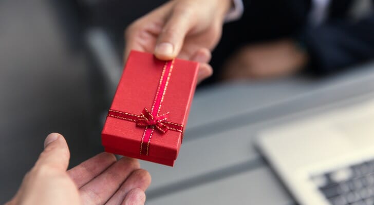 Image shows one person offering a boxed holiday gift to another person; only their hands are visible in the frame. In this study, SmartAsset took a closer look at financial advisors' plans for sending client gifts this year.
