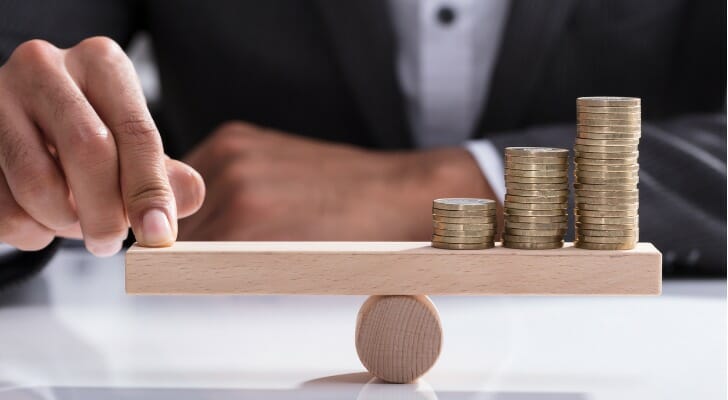 businessperson-balancing-stacked-coins-on-wooden-seesaw-SmartAsset